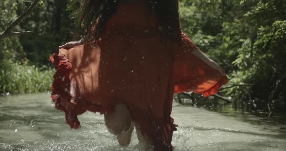 Woman running through water wearing a long red dress