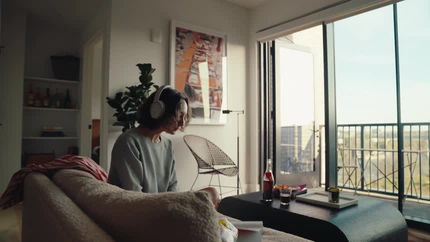 A woman is sitting on her couch listening to music and looking through a book