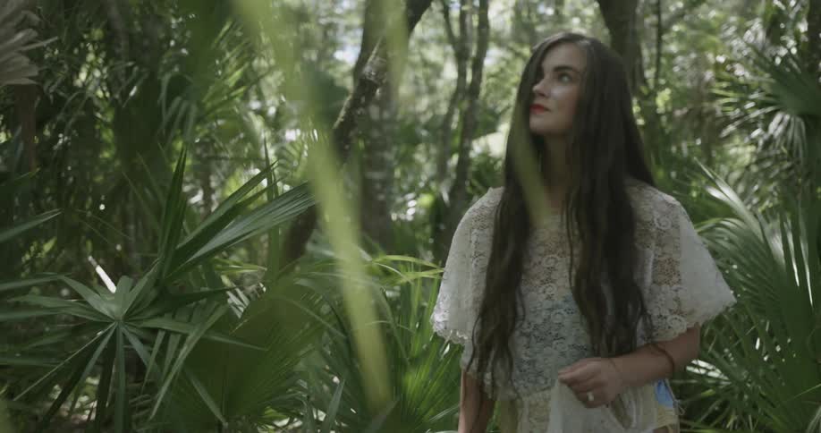 A woman is looking up at the trees around her on a sunny day