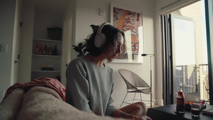 Woman with headphones sitting on the sofa in the living room and eating