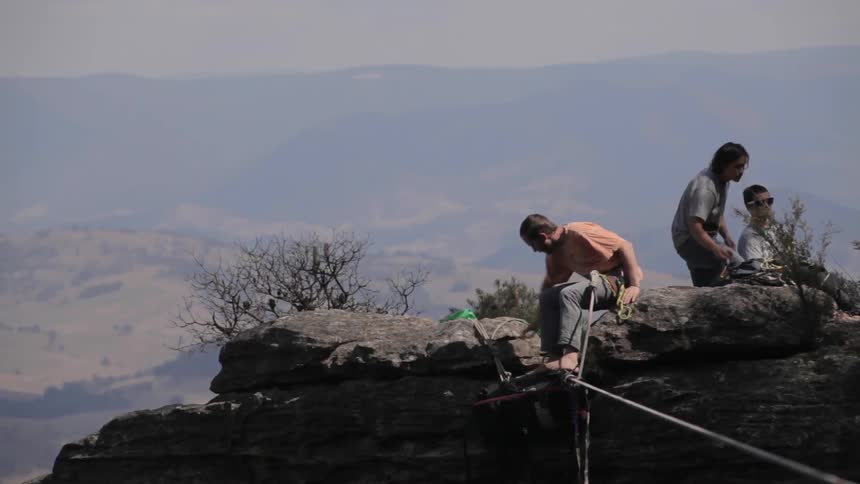 A man secures a rope around his waist while cliffside