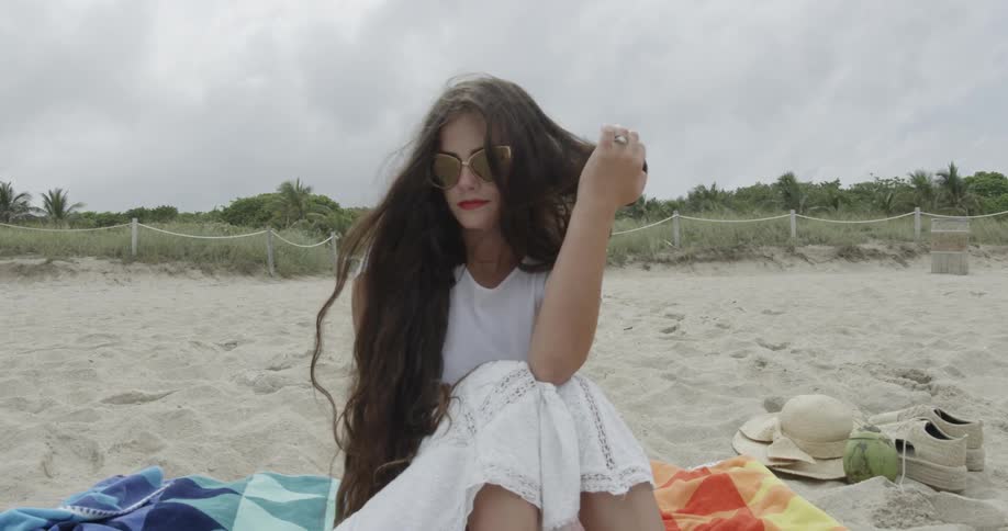 Woman in white dress sitting on towel in the sand