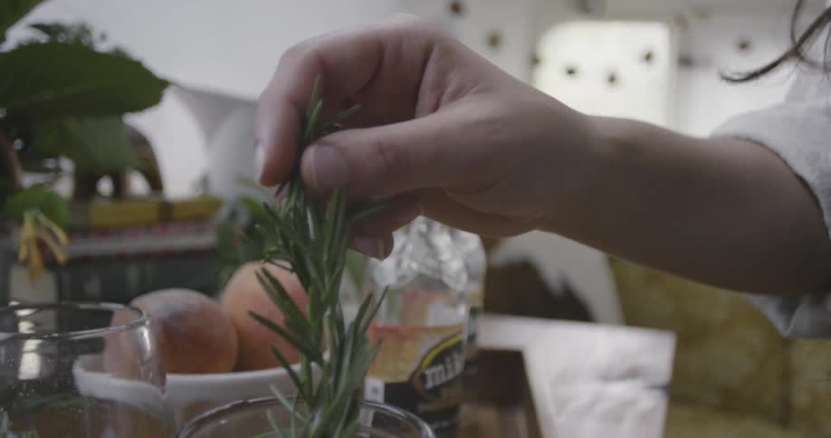 A woman places a sprig of rosemary into a mixed drink