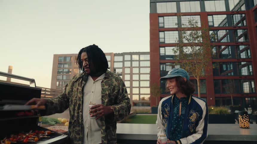 Man drinking beer and talking to a woman while in an outdoor setting having a barbecue