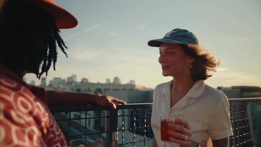 Woman and a man in an elevated environment next to a fence enjoying the landscape of a city in the wind