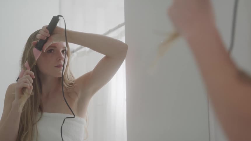 Woman in front of the mirror curling her straight blonde hair