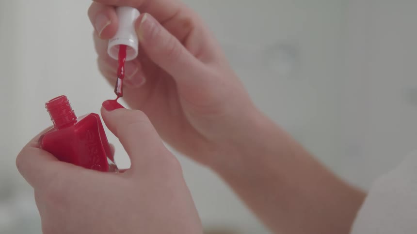 Close up of a pair of hands painting themselves with red nail polish