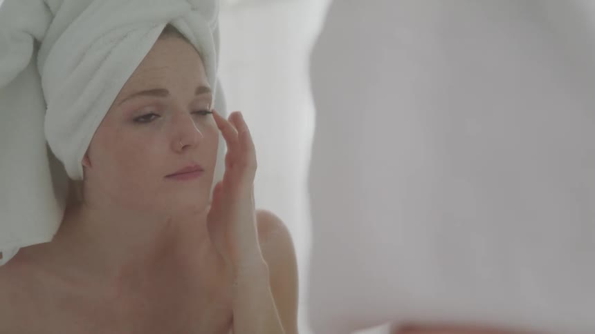 Woman with a towel on her head massaging her face in front of the mirror