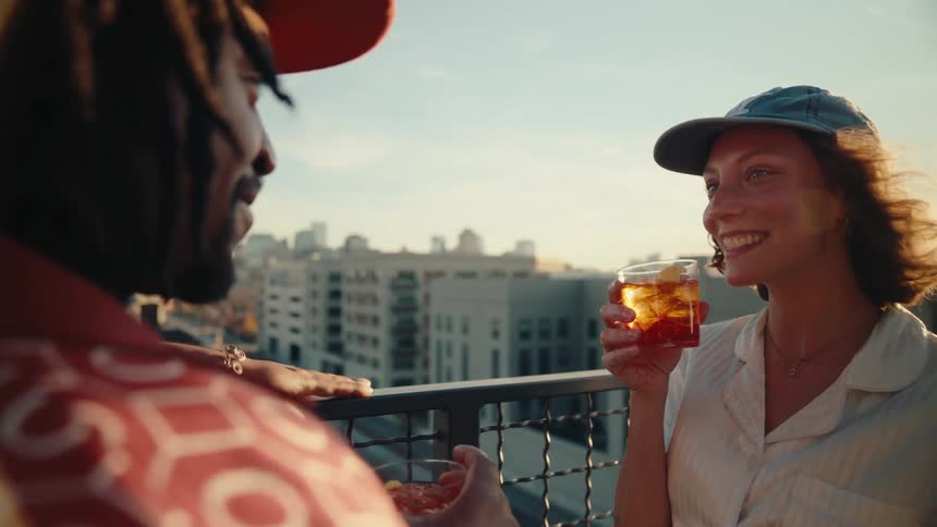 The face of a happy woman wearing a cap who is holding a drink and toasting with a man who is in front of her