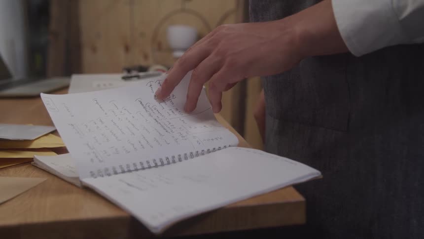 Man wearing an apron stands in an office reading a notebook