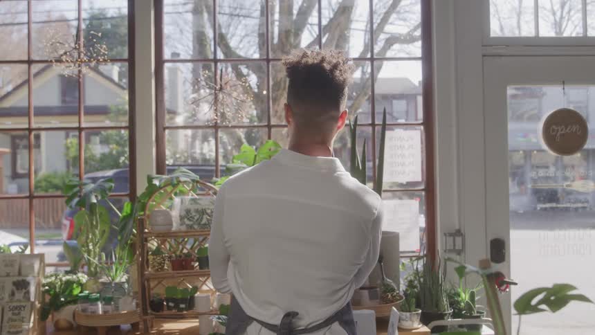 A man is looking at the neighborhood through a large window