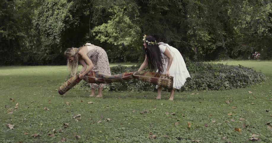 Two women carrying and unrolling a carpet on the grass in a park