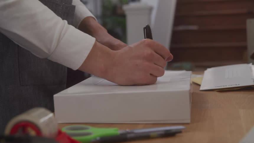 Person stands writing on a box sitting on a table near the base of a staircase