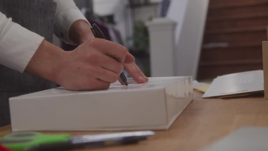 A man is using a pen to write on a cardboard shipping box