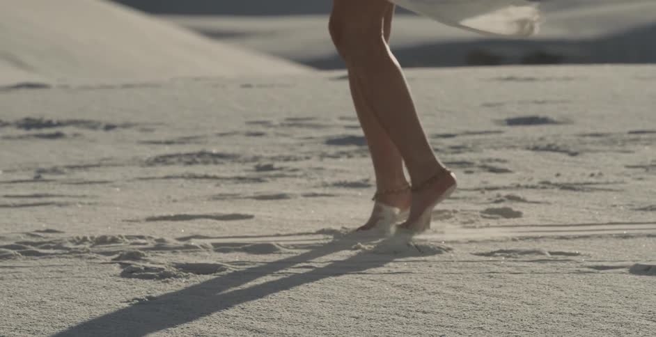 Woman in white dress spinning around in the sand
