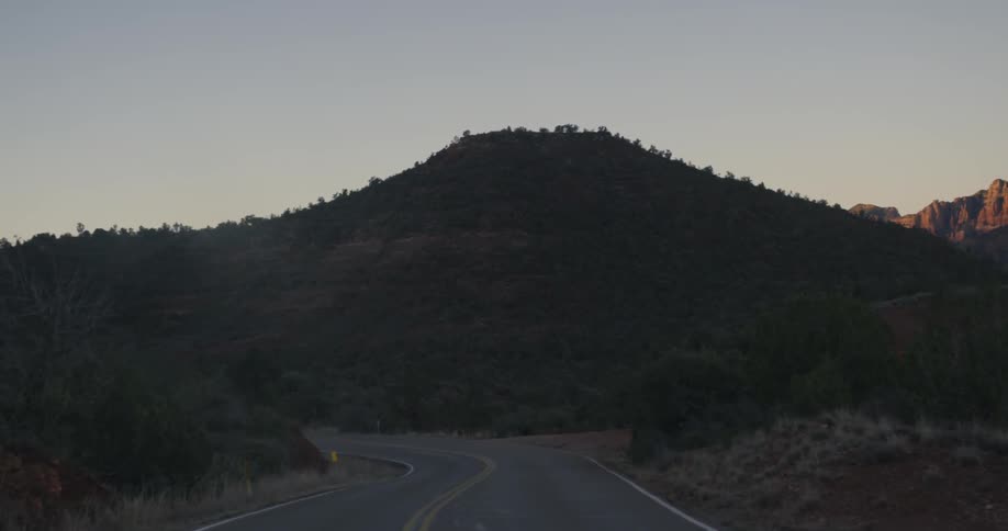 A two lane road that is approaching a mountain