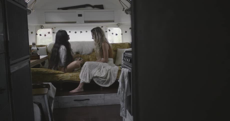 Two women sitting on a couch inside travel trailer are talking