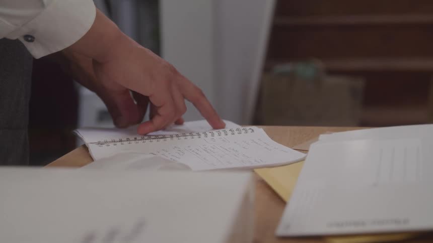 Man standing at a table near the base of a staircase reads a notebook