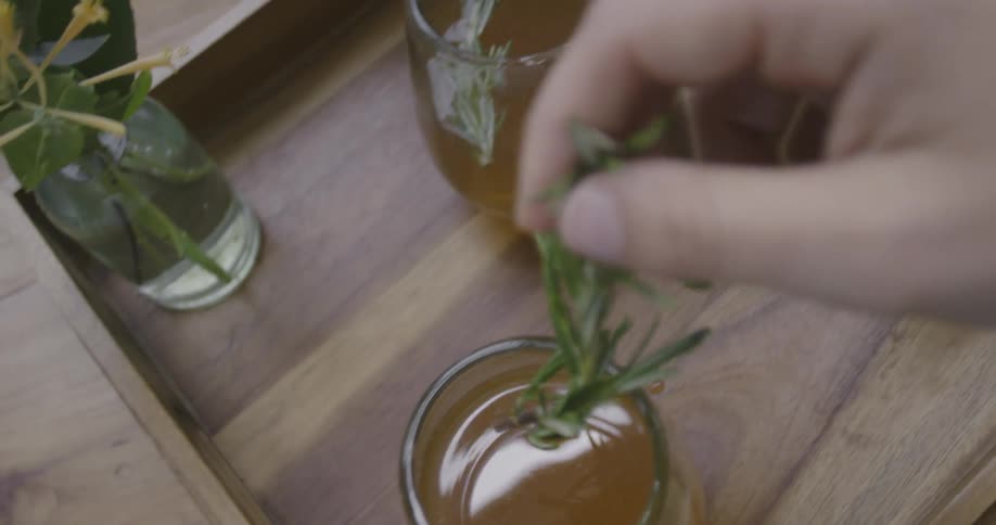 A hand is placing a sprig of rosemary into a drink