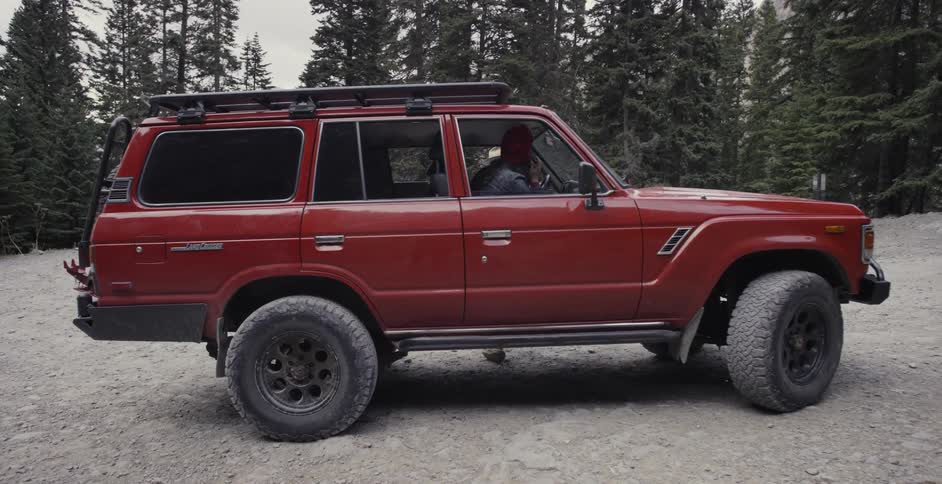 A person is sitting in a red suv parked near a forest