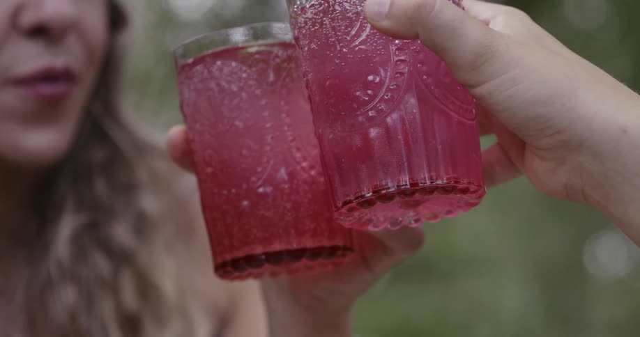 Two people cheersing glasses filled with pink colored beverage