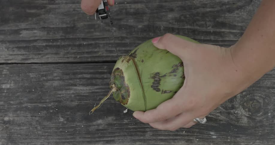 A person is using a knife to cut a green coconut