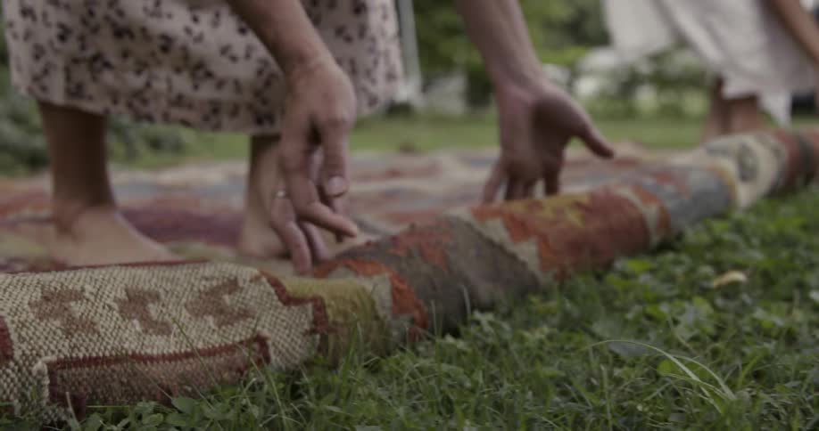 Two women unrolling a rug in a grassy area