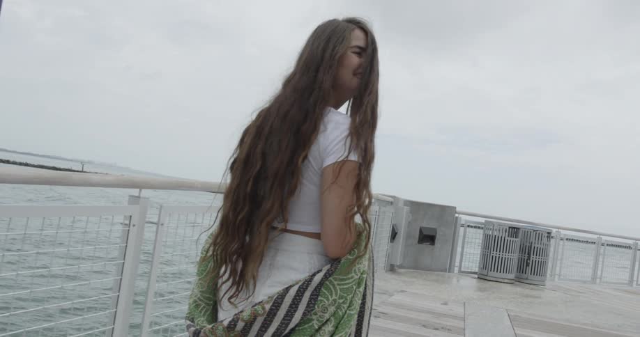 Smiling woman holding a shawl is walking on a pier