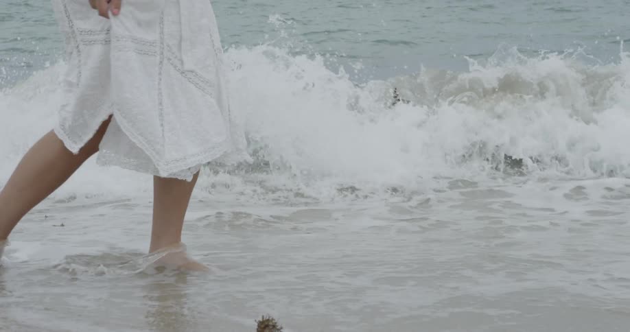 Woman in white dress walking through shallow ocean waves