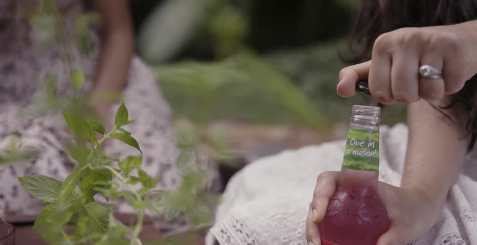 A woman is twisting open the lid of a drink outside during the day