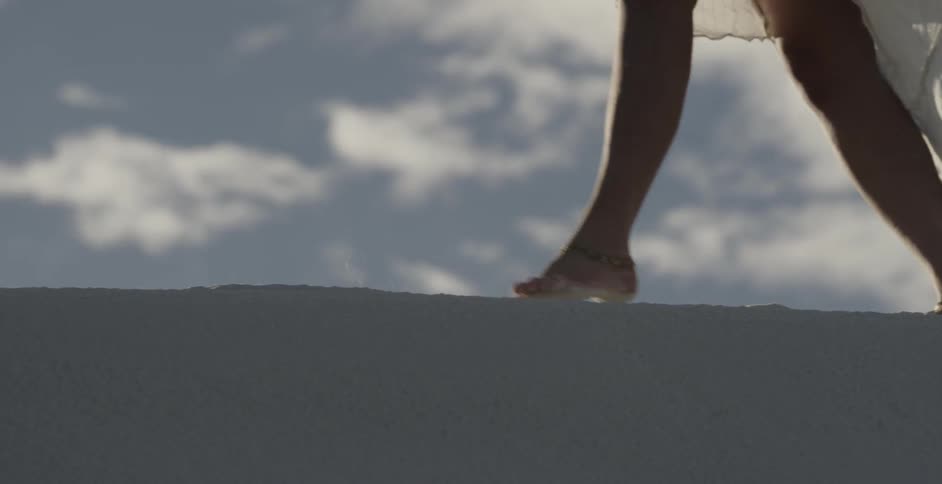 Woman in white dress walking and dragging her feet in the sand