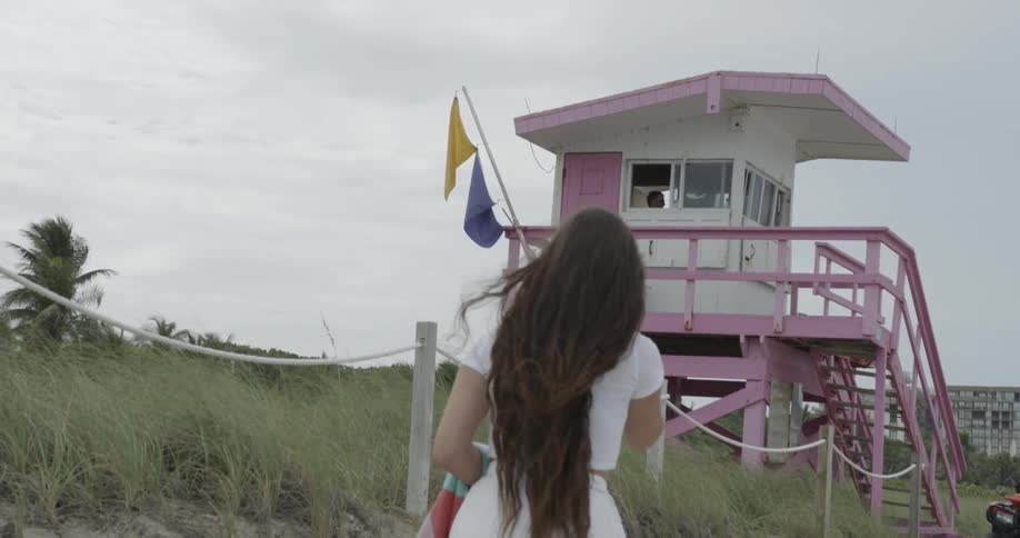 Woman walking towards pink colored lifeguard tower on beach