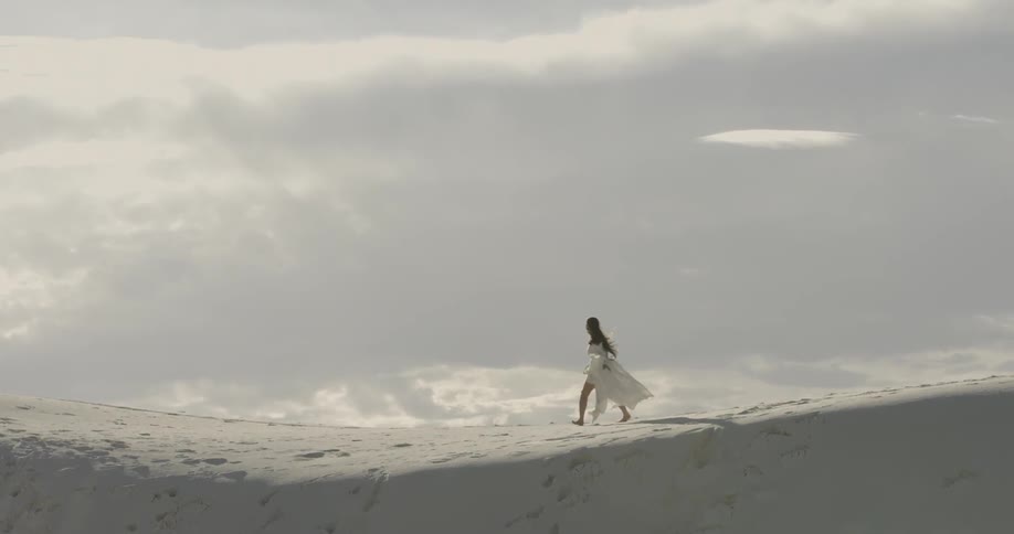 Woman in white dress is skipping across sand