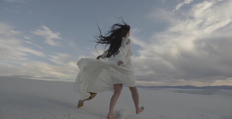 Woman in white dress is skipping across sand