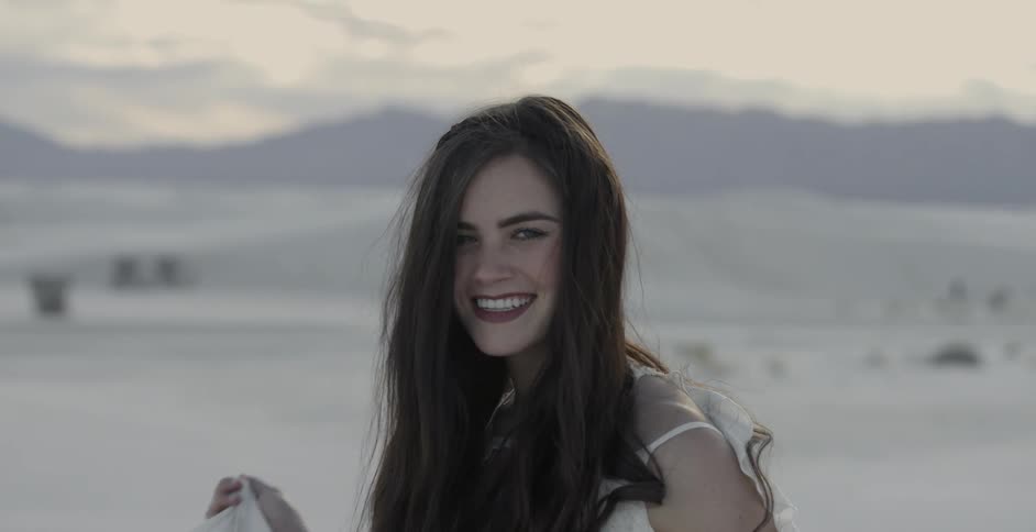 Long-haired brunettes smiling for the camera with mountains in the background