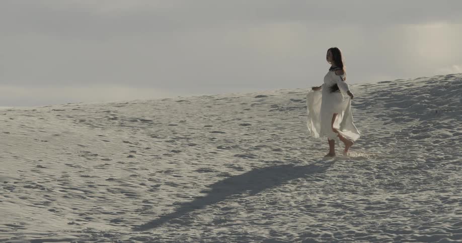 Woman in white dress skipping in the sand