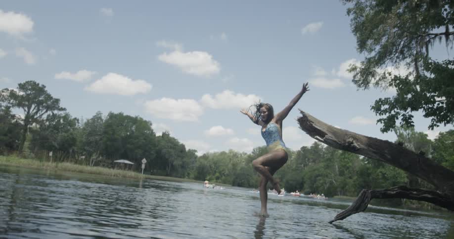 Woman jumping off of a fallen tree branch into water