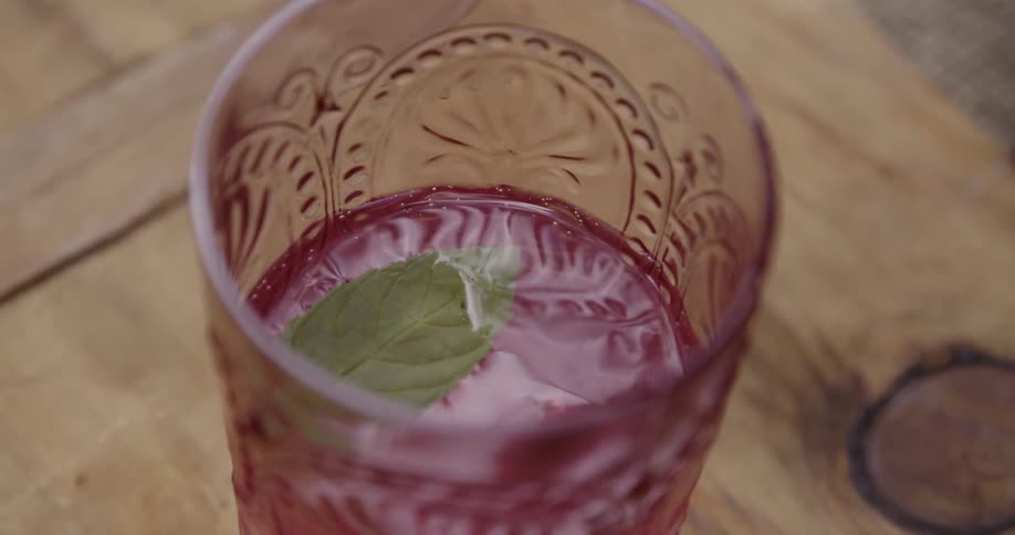 Mint leaf dropping into a glass filled with a pink colored beverage