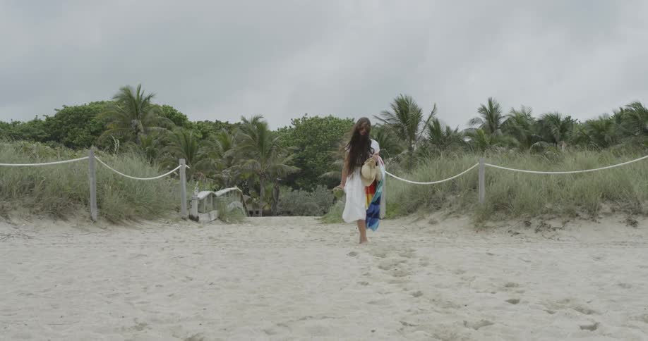 Woman in white dress walking through sand on overcast day