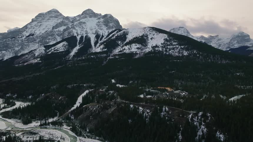 A snow capped mountain range overlooking a forested landscape a winding river and the Kananaskis hotel and conference center