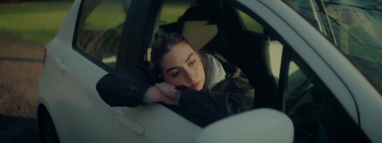 A woman lays her head on the open window of a car