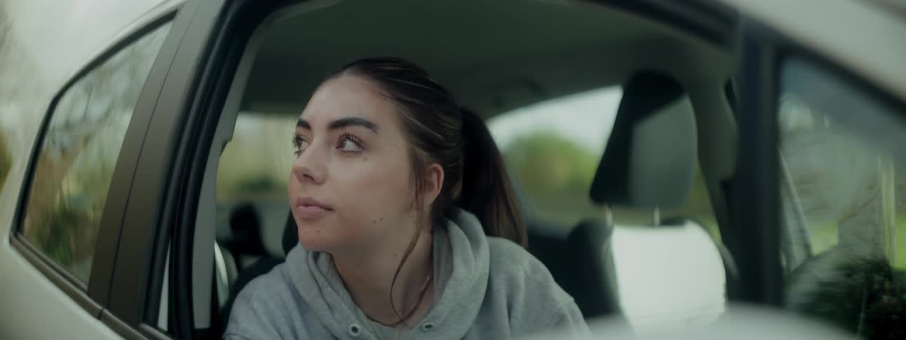 Woman sitting in a parked vehicle rolls down the window and smiles slightly while looking out