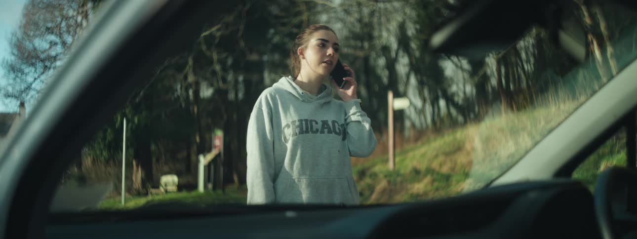 Woman answering a call on a smartphone next to a car