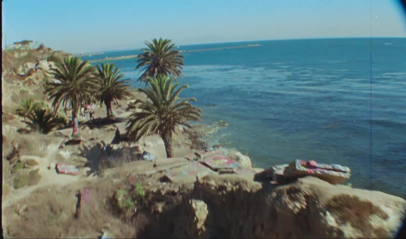 An aerial view of people near coastal cliffs covered in graffiti on a tropical setting