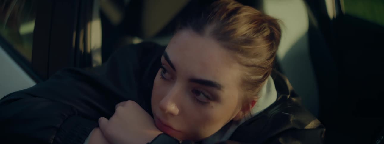 A young woman seemingly contemplative rests her head on her arm inside a vehicle