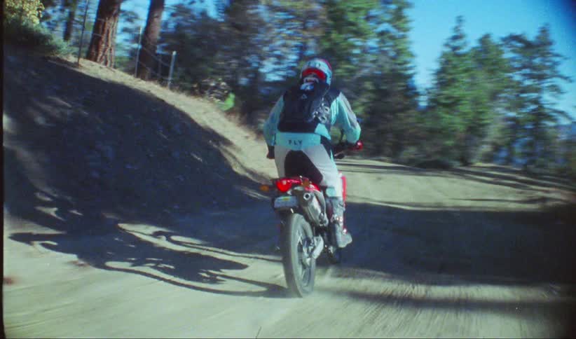 Motorcyclist passes patches of snow while riding along a path passing over a forested slope on a sunny winter day