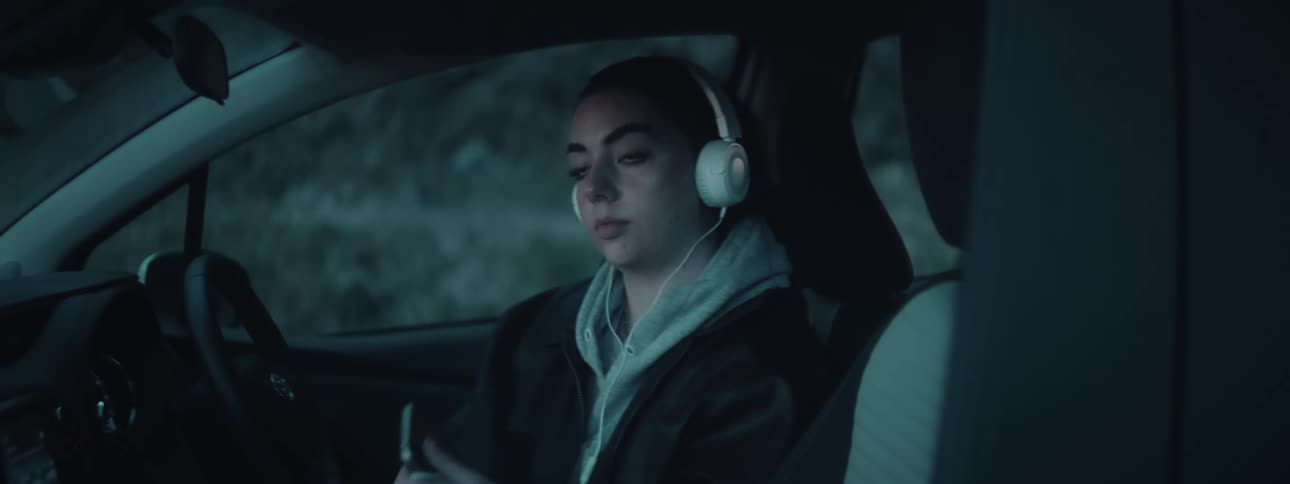 A woman in a car puts on headphones preparing to listen to something