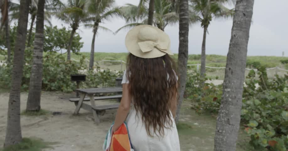A woman is walking toward a picnic table surrounded by palm trees