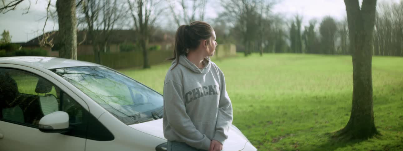 A teenager is leaning on the car