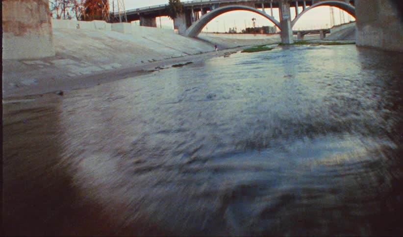 A man dances on a riverbed near the bridge at sunset